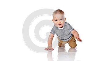 Happy and keen infant boy toddler in t-shirt and green pants is crawling on all fours on white with copy space