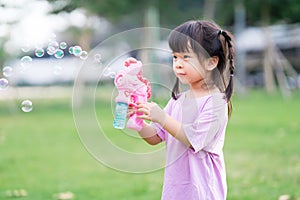 Happy kid 4 year old has fun playing with a pink bubble gun. Child is excited by the bubbles that come out.