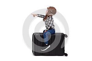 Kid Asian boy sitting on a black suitcase and pointing finger to copy space isolated over white background, Dreams of travel