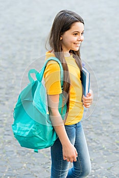 Happy kid back to school carrying backpack and book in casual fashion style outdoors, knowledge