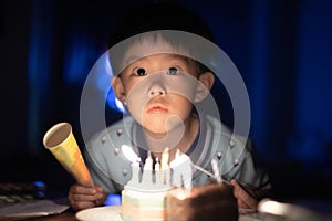 A happy kid is blowing candles on his birthday cake at his birthday party night