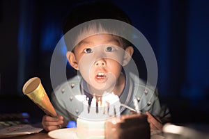 A happy kid is blowing candles on his birthday cake at his birthday party night