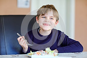 Happy kid boy eating fresh salad with tomato, cucumber and different vegetables as meal or snack. Healthy child enjoying