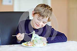 Happy kid boy eating fresh salad with tomato, cucumber and different vegetables as meal or snack. Healthy child enjoying