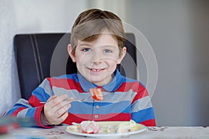 Happy kid boy eating fresh salad with tomato, cucumber and different vegetables as meal or snack. Healthy child enjoying