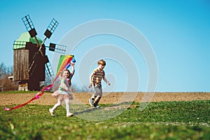 Happy kid boy and girl playing with kite over wind turbine farm and green renewable energy. Concept of sustainability