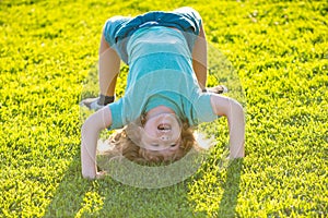 Happy kid boy girl standing upside down on her head on grass in summer day.