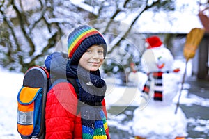 Happy kid boy with glasses having fun with snow on way to school, elementary class