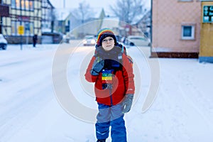 Happy kid boy with glasses having fun with snow on way to school, elementary class