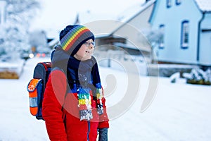 Happy kid boy with glasses having fun with snow on way to school, elementary class