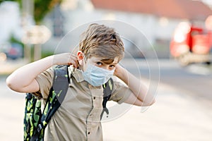 Happy kid boy with glasses and medical mask due to corona virus covid pandemic. Schoolkid with satchel waiting for bus on the way