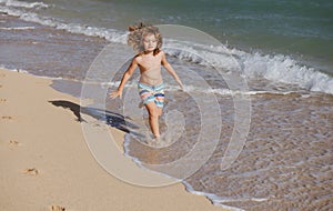 Happy kid boy have fun on tropical sea beach. Funny child run with splashes by water pool along surf edge. Kids activity