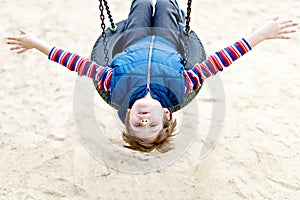 Happy kid boy having fun with chain swing on outdoor playground. child swinging on warm sunny spring or autumn day