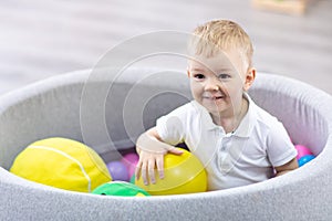 Happy kid boy having fun indoor in play center. Child playing with colorful balls in playground ball pool.