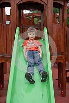 Happy kid boy having fun and sliding on outdoor playground