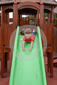 Happy kid boy having fun and sliding on outdoor playground