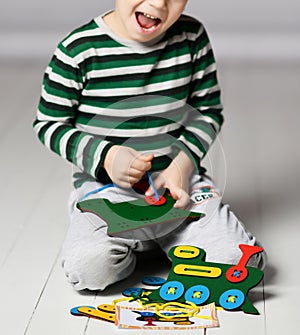 Happy kid boy plays educational game with wooden colorful train and laces