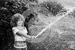 Happy kid boy pours water from a hose. American kids childhood. Child watering flowers in garden. Home gardening.