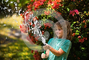 Happy kid boy pours water from a hose. American kids childhood. Child watering flowers in garden. Home gardening.