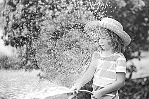 Happy kid boy pours water from a hose. Child watering flowers in garden. Home gardening.