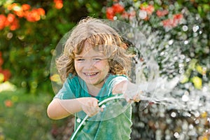 Happy kid boy pours water from a hose. Child watering flowers in garden. Home gardening.