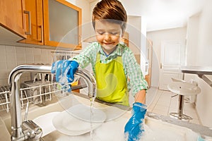 Happy kid boy rinsing dishes in the sink