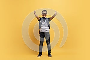 Happy kid boy schooler showing thumb ups, isolated on yellow