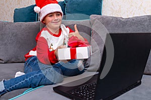 Happy kid boy shows thumb up Christmas through a video call with friends showing gift box