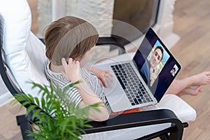 Happy kid boy sit on chair with computer using laptop having a video call with father. Child talking to his dad and dog on video