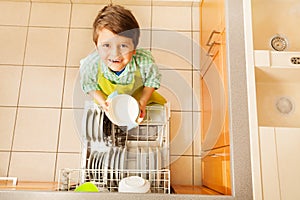 Happy kid boy taking out dishes from dishwasher photo