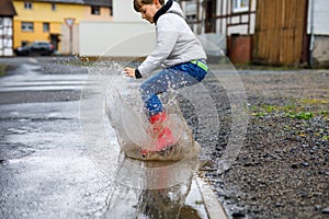 Happy kid boy wearing red rain boots and walking during sleet and rain on rainy cloudy day. Child in colorful casual