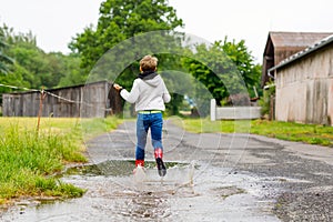 Happy kid boy wearing red rain boots and walking during sleet and rain on rainy cloudy day. Child in colorful casual