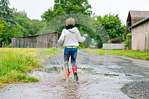 Happy kid boy wearing red rain boots and walking during sleet and rain on rainy cloudy day. Child in colorful casual