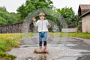 Happy kid boy wearing red rain boots and walking during sleet and rain on rainy cloudy day. Child in colorful casual