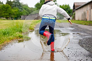 Happy kid boy wearing red rain boots and walking during sleet and rain on rainy cloudy day. Child in colorful casual