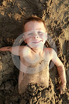 Happy kid buried in sand on beach