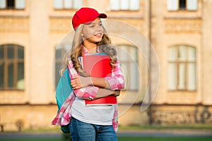 Happy kid in casual fashion style hold study books carrying school bag with pensive look outdoors, future, copy space