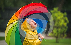 happy kid catching rain drops in park. Funny little girl playing under the autumn rain. Kid wearing yellow waterproof