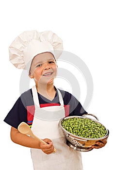 Happy kid with chef hat and a bowl of green peas