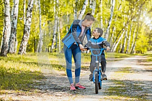 Happy kid cyclist learning to ride a bike with mom in the sunny forest on a bike