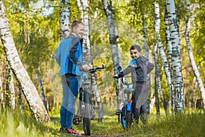 Happy kid cyclist learning to ride a bike with mom in the sunny forest on a bike