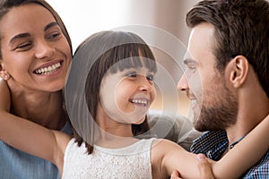 Happy kid daughter embracing parents looking at smiling mom