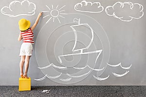 Happy kid draws a chalk ship on the wall