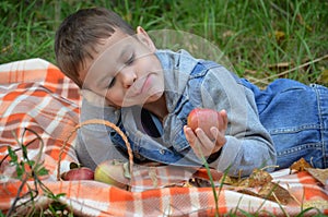 Happy kid eating fruits. happy cute child boy eating an apple. lies on a coverlet in an autumn park