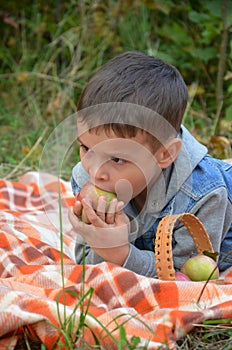 Happy kid eating fruits. happy cute child boy eating an apple. lies on a coverlet in an autumn park