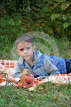 Happy kid eating fruits. happy cute child boy eating an apple. lies on a coverlet in an autumn park