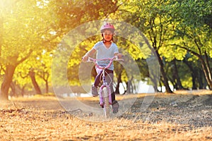 Happy kid girl of 7 years having fun in autumn park with a bicycle on beautiful fall day. Active child wearing bike helmet