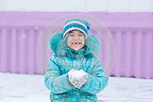 Happy kid girl child outdoors in winter playing holding snow