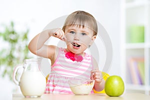 Happy kid girl eating food itself with spoon