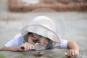 Happy kid girl exploring nature with a magnifying glass and a snail. He having fun in the garden. The concept of the kid is ready
